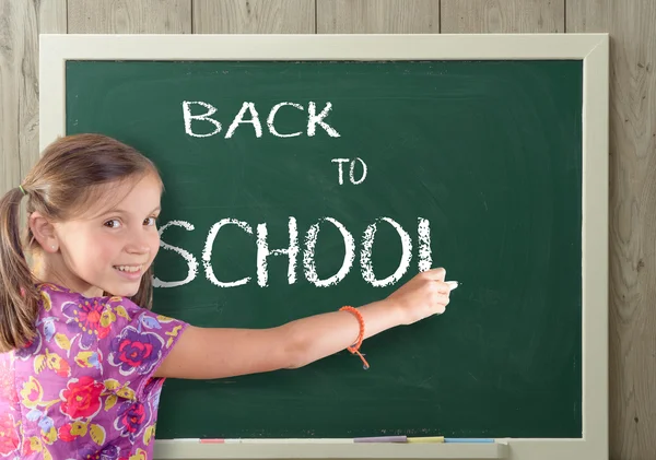 Menina bonita escrevendo de volta para a escola no quadro negro — Fotografia de Stock