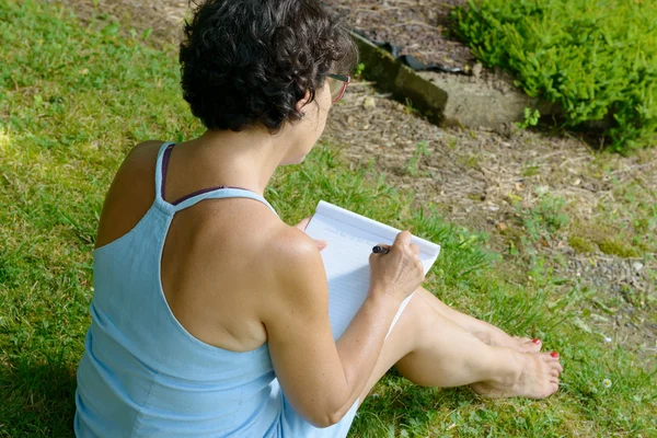 Rijpe vrouw schrijft een brief in de tuin — Stockfoto