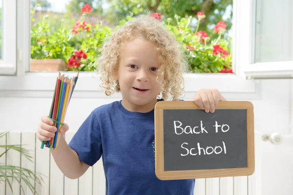 Pojken håller en griffeltavla som skrivit tillbaka till skolan — Stockfoto