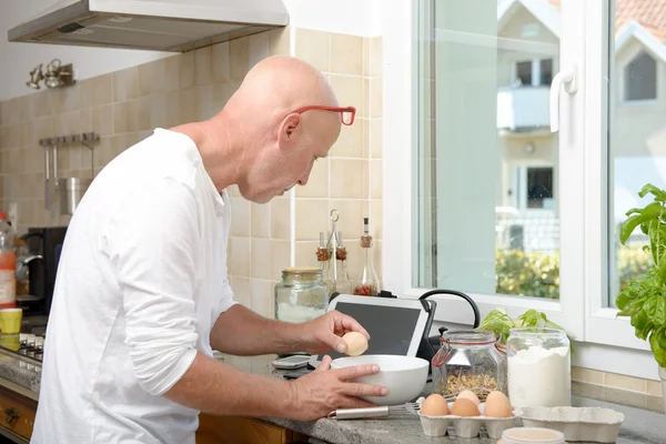 Senior man cooking in the kitchen at home with tablet — Stock Photo, Image