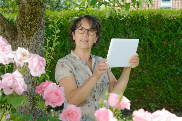 Mature woman with a tablet in the garden — Stock Photo, Image