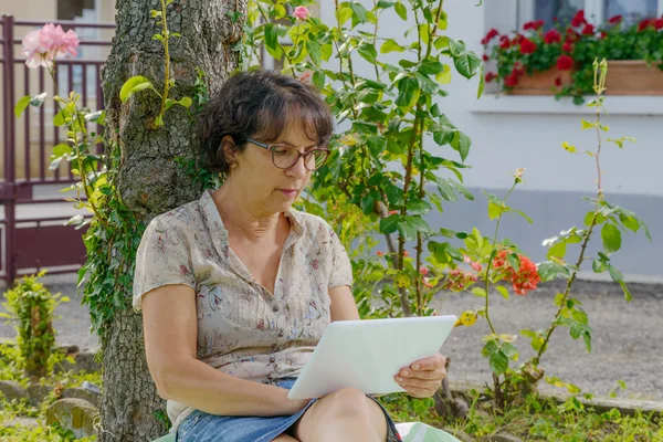 Mature woman sitting with a tablet in the garden — Stock Photo, Image