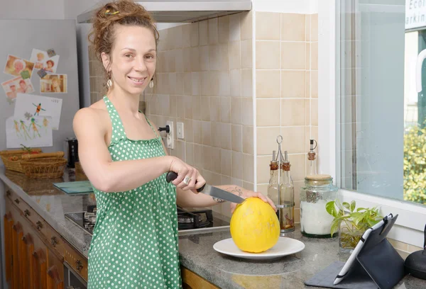 Mujer joven cortando un melón en la cocina — Foto de Stock