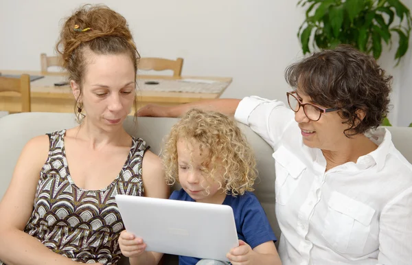 Child and his mother with grandmother play with tablet — Stock Photo, Image