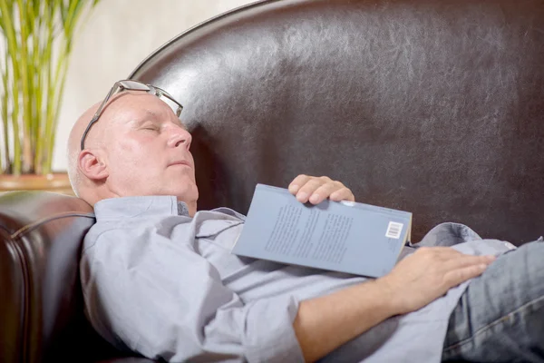 Un anciano con un libro en un sofá dormido —  Fotos de Stock