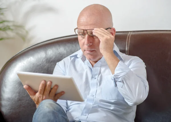 A senior with glasses looks at a digital tablet — Stock Photo, Image