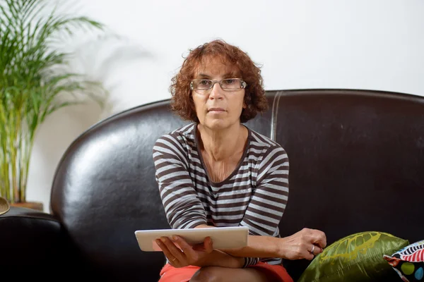 Una mujer mayor en un sofá con una tableta digital —  Fotos de Stock