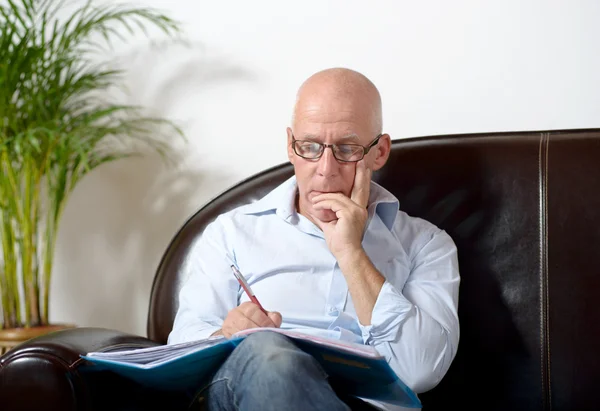 A senior man sitting in a sofa taking notes — Stock Photo, Image