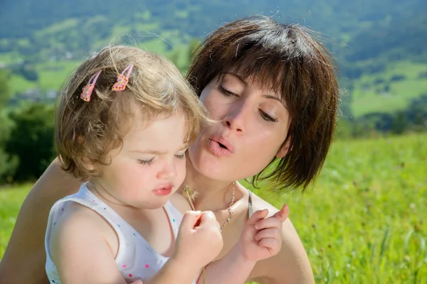 A beautiful mom and daughter play with a flower in nature — Stock Photo, Image