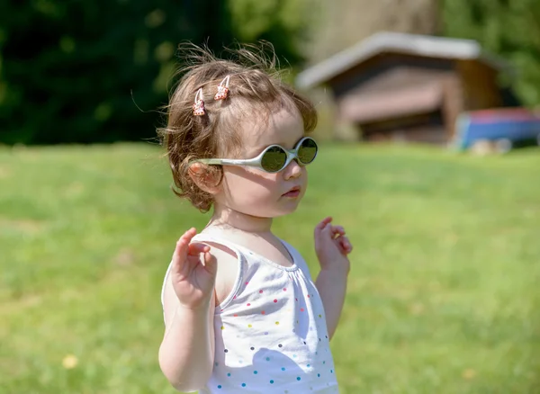 A little girl in the garden with sunglasses — Stock Photo, Image