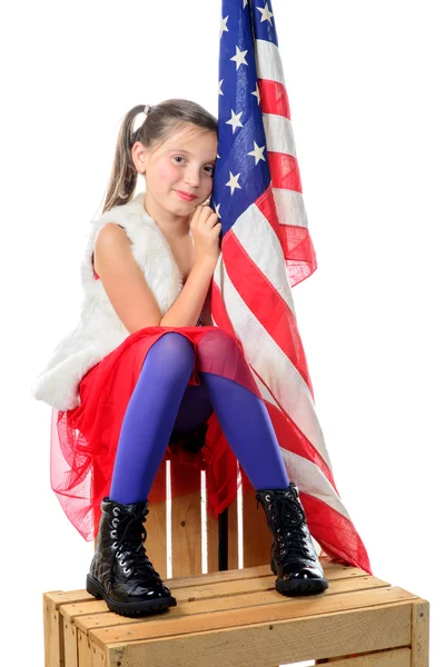 Ein hübsches kleines Mädchen sitzt auf einer Schachtel mit einer amerikanischen Flagge — Stockfoto