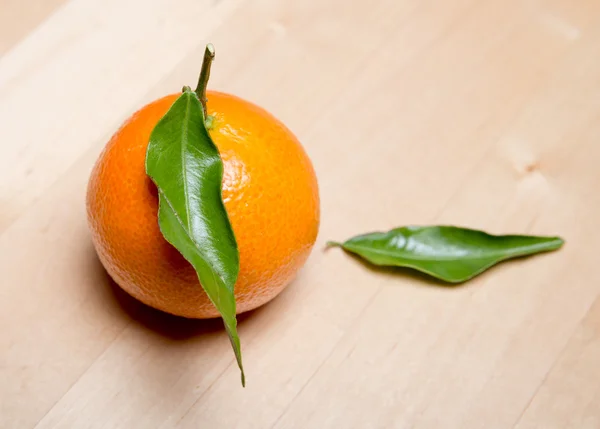 Mandarin with two green leaves on a light wooden table — Stock Photo, Image