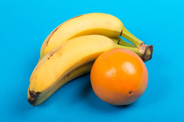 Banane și o portocală pe fundal albastru — Fotografie, imagine de stoc