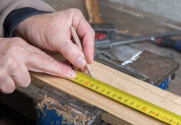 A worker measuring a board with a tape measure — Stock Photo, Image