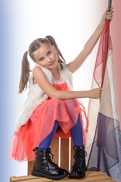 Ein hübsches kleines Mädchen sitzt auf einer Schachtel mit einer französischen Flagge — Stockfoto