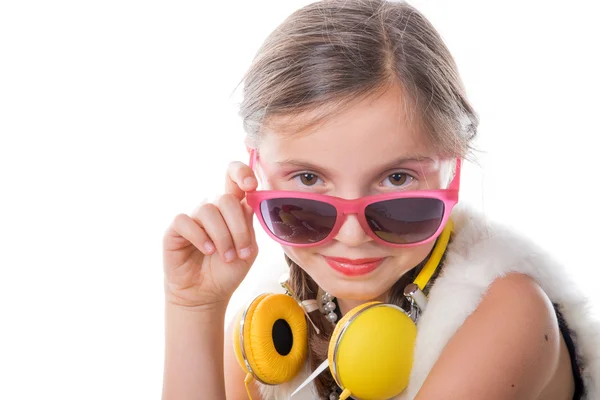 En söt liten flicka med rosa glas och gula hörlurar — Stockfoto