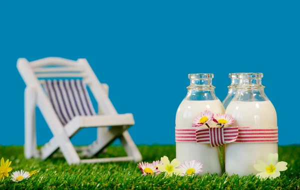Three bottles of milk with a lounge chair in the grass — Stock Photo, Image
