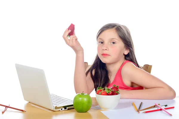 Mała dziewczynka siedzi przy biurku, jedząc truskawki — Zdjęcie stockowe