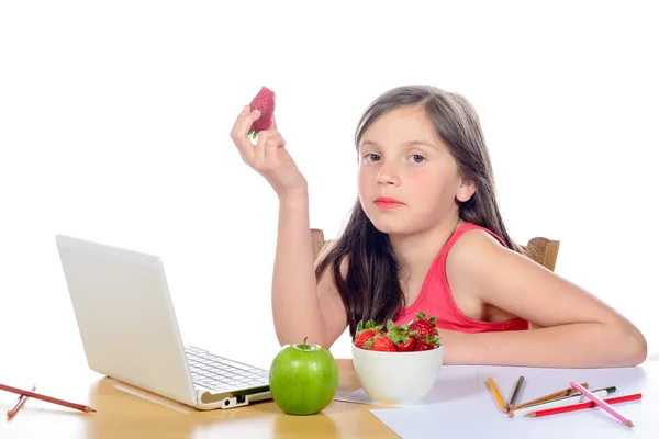 Een klein meisje zit aan zijn Bureau eten van een aardbei — Stockfoto