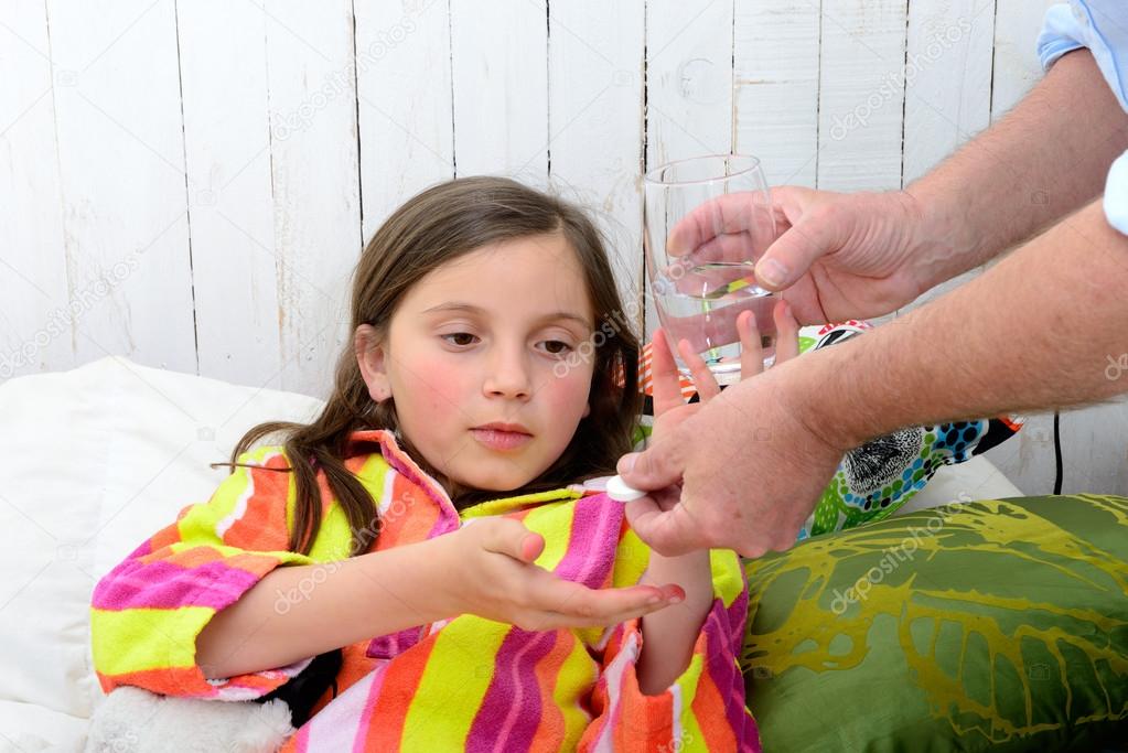 a little girl in bed taking tablet