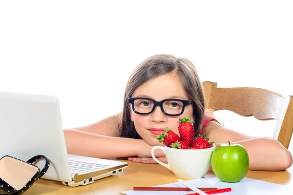 Een klein meisje zit aan zijn bureau met een kom van aardbeien een — Stockfoto