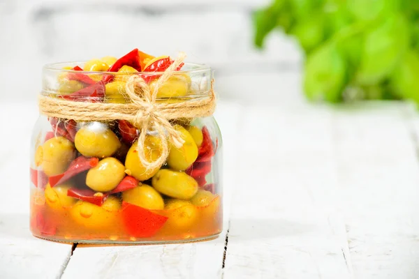 Tarro de vidrio con aceitunas y pimientos sobre mesa blanca —  Fotos de Stock