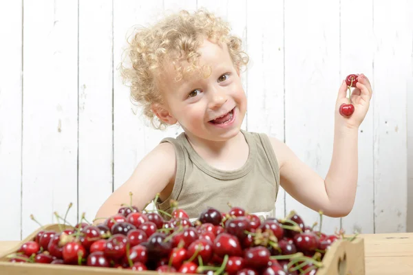 Um pequeno menino loiro comendo cerejas — Fotografia de Stock