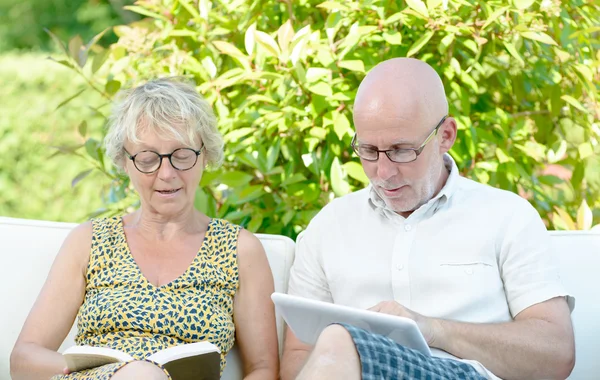 A man looks at a digital tablet and his wife is reading a book — Stock Photo, Image