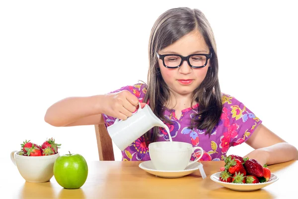 En liten flicka häller mjölk i en kopp — Stockfoto