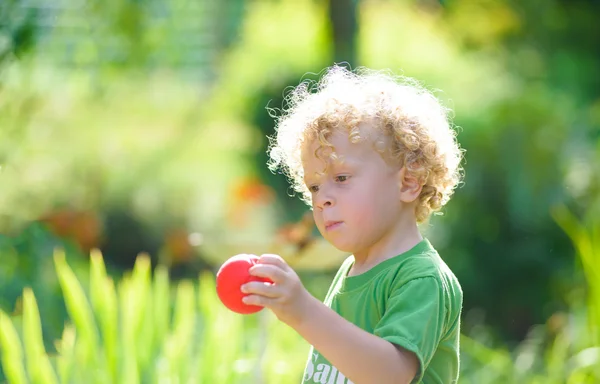 Un niño rubio con una pequeña bola roja — Foto de Stock