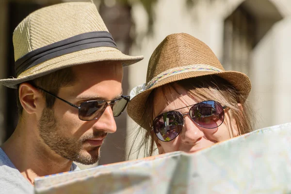 Um jovem casal com chapéus, olhando para um mapa — Fotografia de Stock