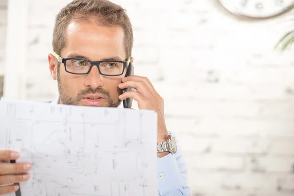 En ung man med glasögon läser en plan och telefon — Stockfoto