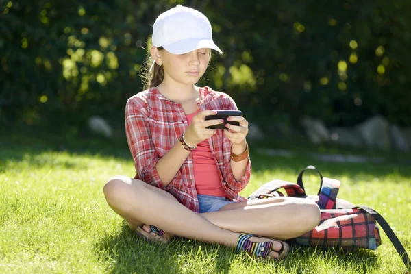 Una bambina seduta nell'erba che gioca con un telefono — Foto Stock