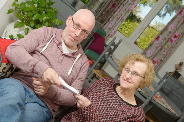 A mother and her adult son looking paper on a sofa — Stock Photo, Image