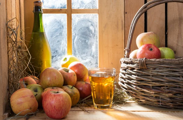 Botella y vaso de sidra con manzanas cerca de la ventana — Foto de Stock
