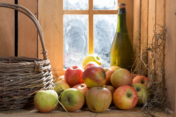 Fles en glas cider met appels in de buurt van het venster — Stockfoto