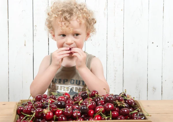 Mladý kudrnatý blonďák jíst třešně — Stock fotografie