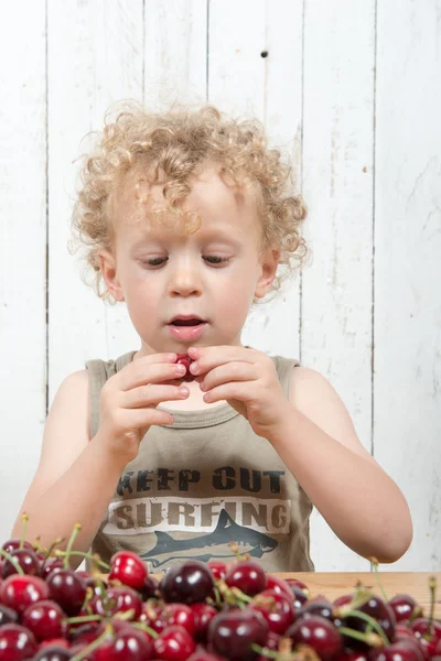 Een jonge blonde krullend jongen kersen eten — Stockfoto