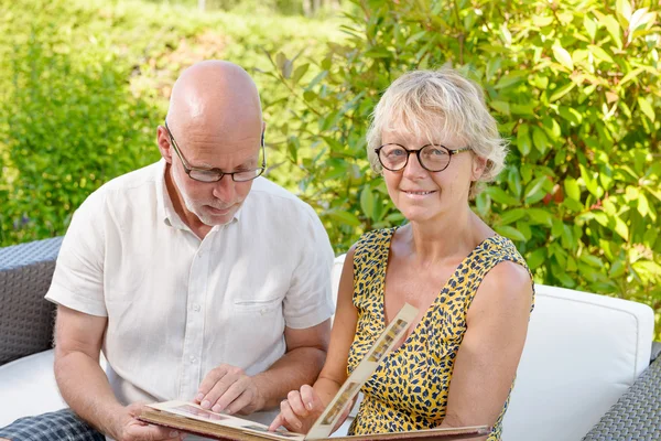 Senior couple looking at a picture book, sitting in a sofa — Stock Photo, Image