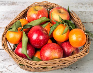 Elmalar ve portakallar dahil bir sepet meyve. Elmalar kırmızı ve portakallar turuncu. Sepet ahşap bir masanın üzerinde.