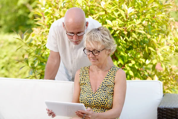 Middle age couple, smiling, using a tablet in their garden — Stock Photo, Image