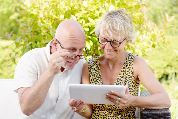 Middle age couple, smiling, using a tablet in their garden — Stock Photo, Image