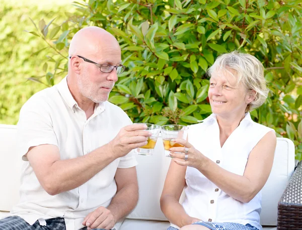 Senior couple sitting in a sofa with a glass in hand — Stock Photo, Image