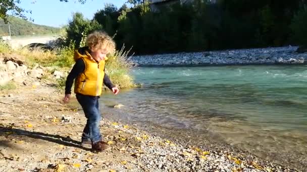 Liten blond pojke leker nära en flod — Stockvideo