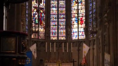 Üç uzun vitraylı pencere, canlı bir ortaçağ sanatı sergiliyor. Her paneli kırmızı ve mavi şekiller dolduruyor. Renkli camların arasından ışık akıyor..