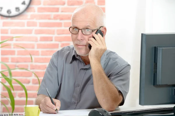 Mellersta åldern affärsman sitter vid skrivbordet talar i mobiltelefon — Stockfoto