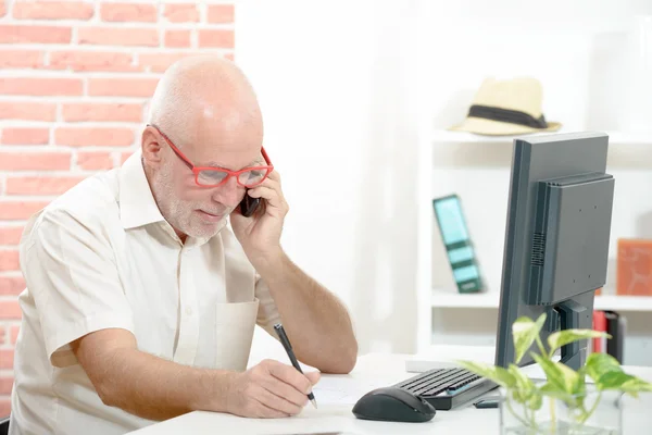 Бизнесмен средних лет сидит за столом и разговаривает по мобильному телефону — стоковое фото