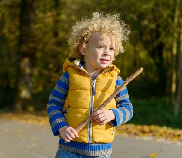 En liten blond pojke leker med en pinne — Stockfoto