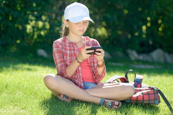 彼の携帯電話で遊んで芝生の上に座っている女子高生 — ストック写真