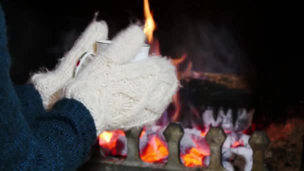 Manteniendo el calor junto a la chimenea con una taza de té caliente . — Vídeo de stock